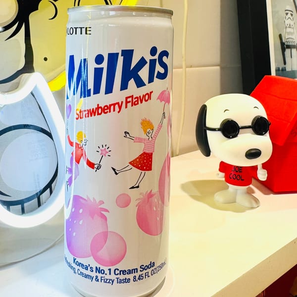 A can of Lotte Milkis Strawberry Flavor soda next to a Joe Cool Snoopy figurine.