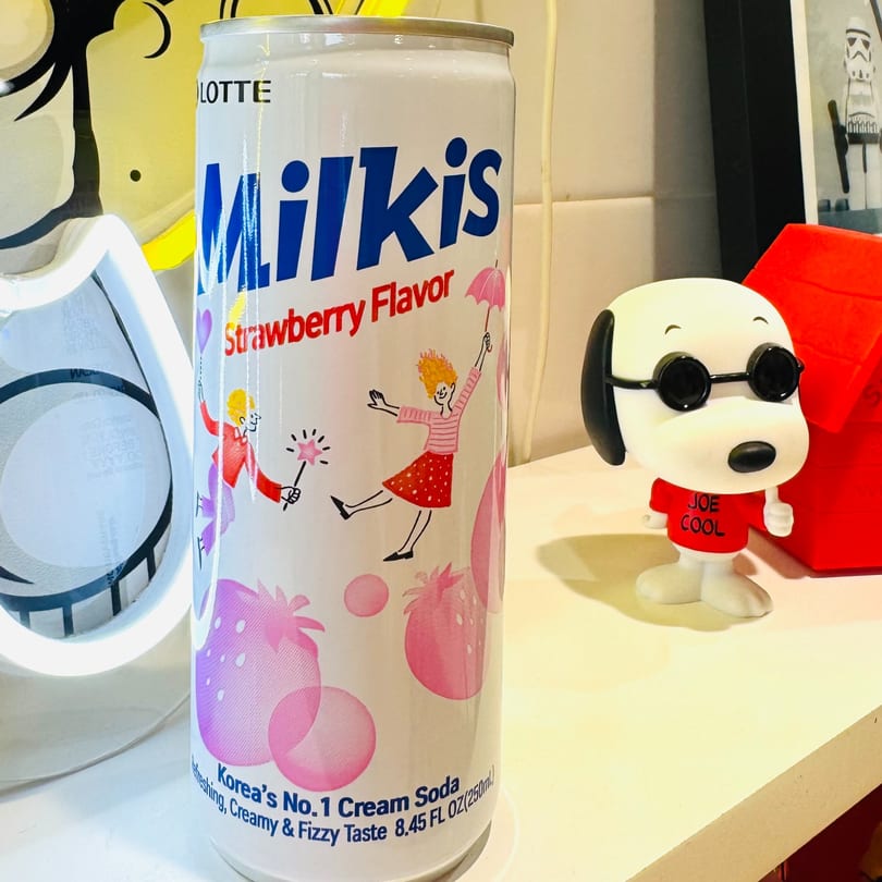 A can of Lotte Milkis Strawberry Flavor soda next to a Joe Cool Snoopy figurine.