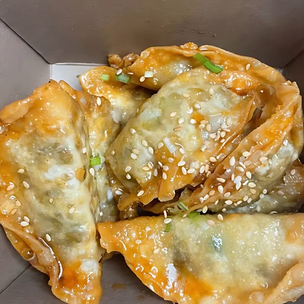 Noori Chicken's Korean fried dumplings, glistening with sauce, sesame seeds, and green onions in a takeout box.